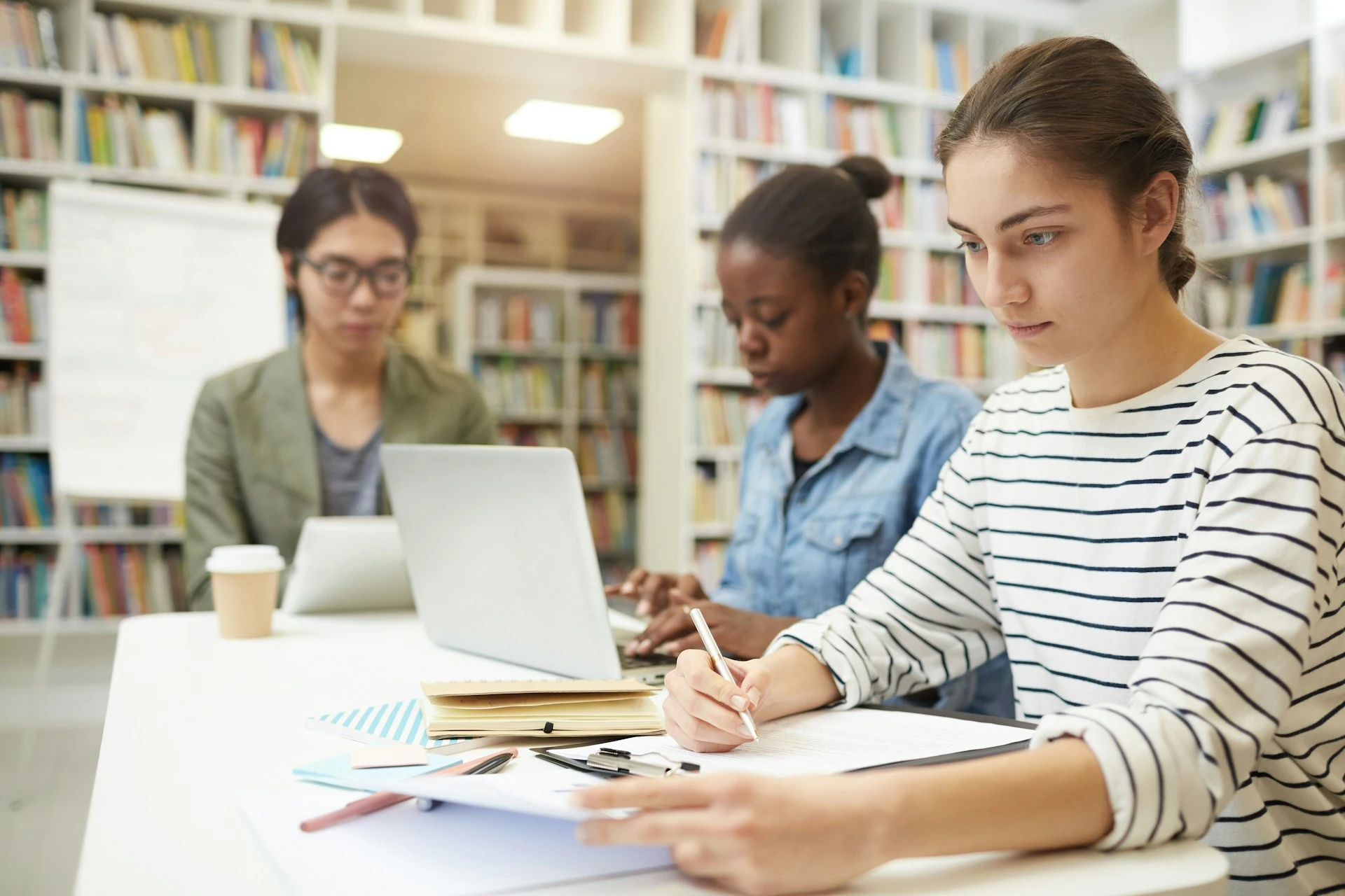 Three students study at a library table.