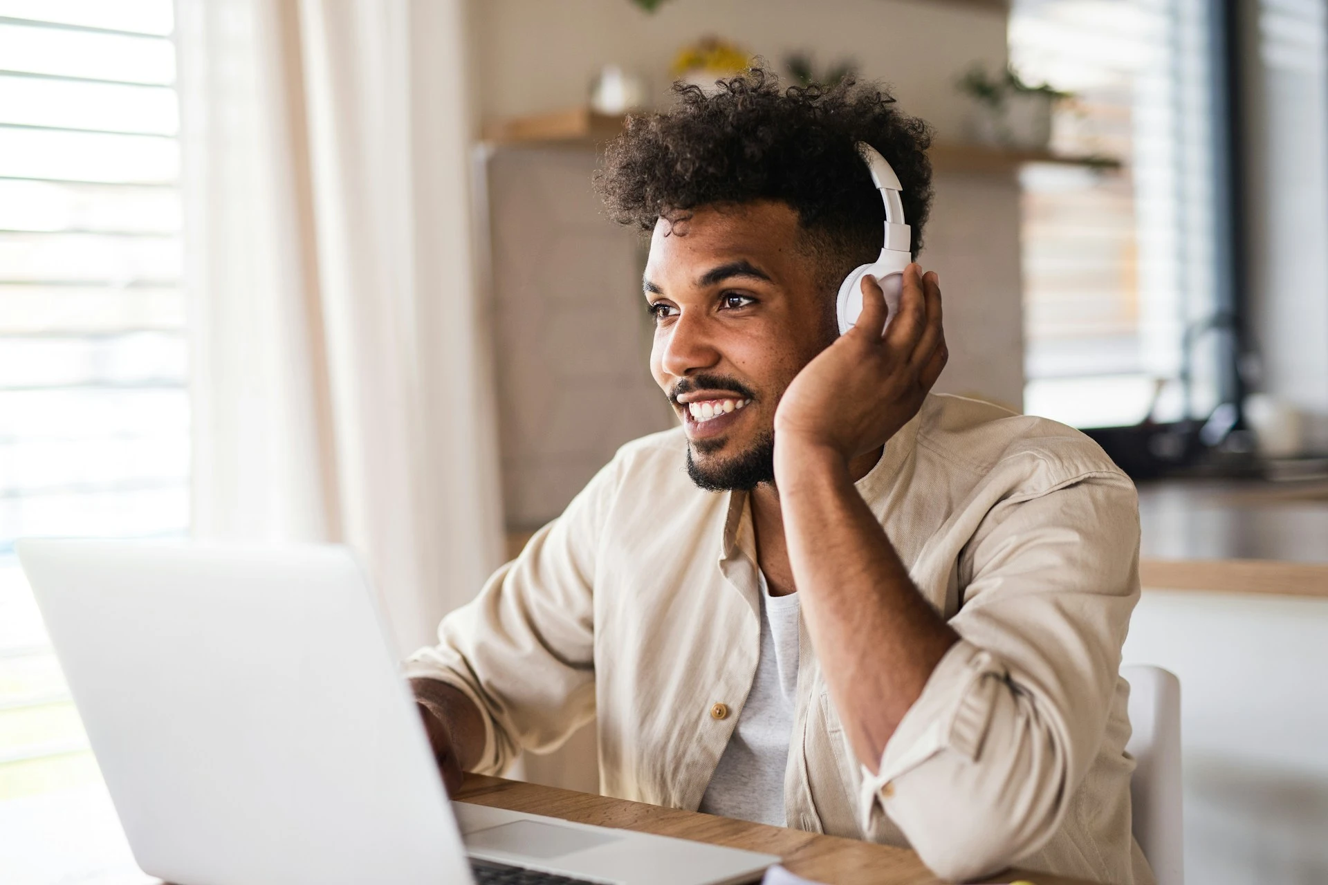  A smiling person with headphones on looks at a laptop screen.