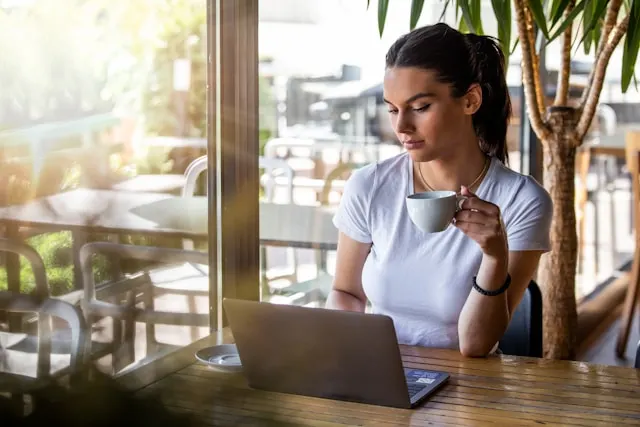 Woman working on a laptop while holding a cup.