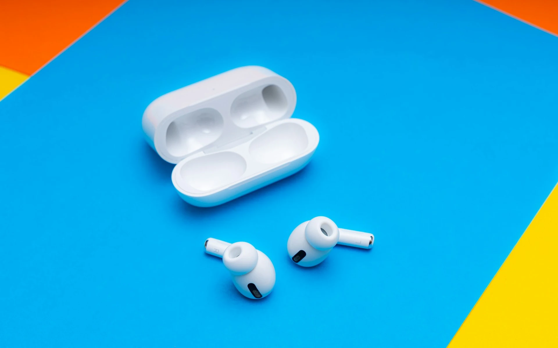 Apple AirPods Pro and their open white charging case resting on a blue background.