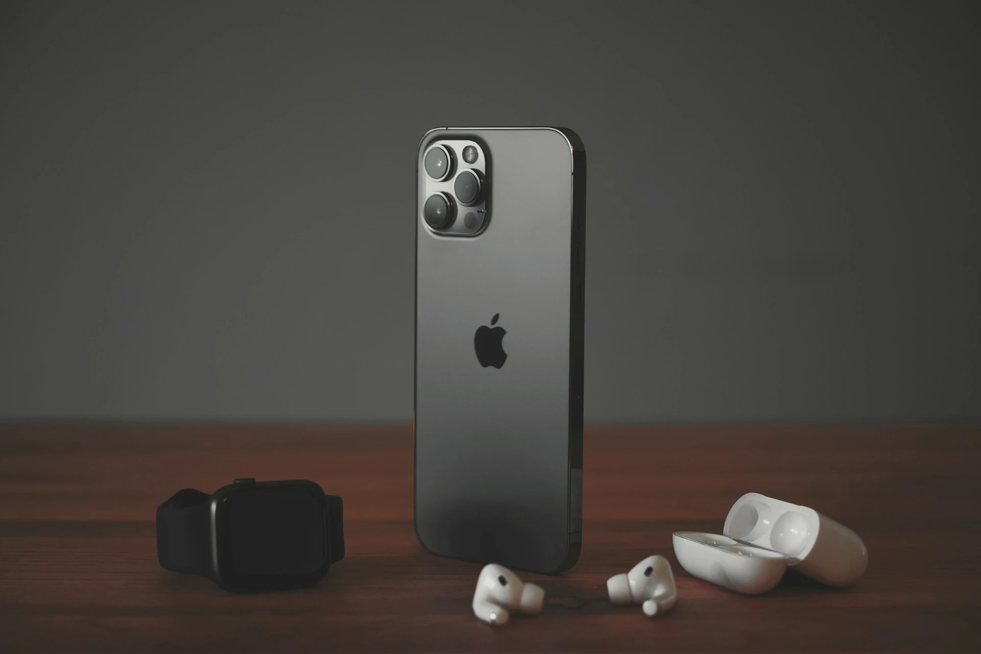 An iPhone, Apple Watch, and AirPods are arranged on a wooden table.