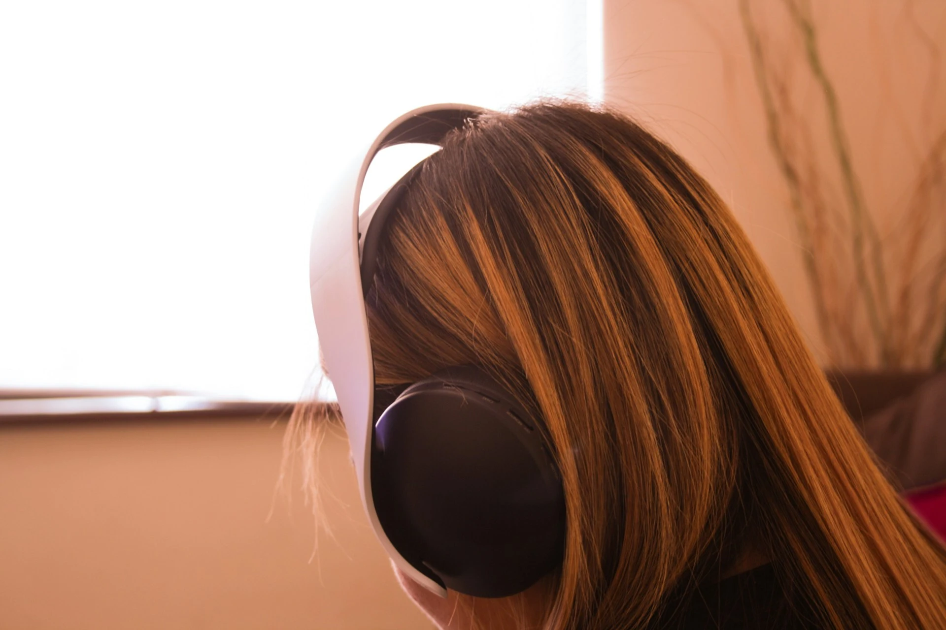 Back view of a person with long highlighted hair wearing white over-ear headphones.