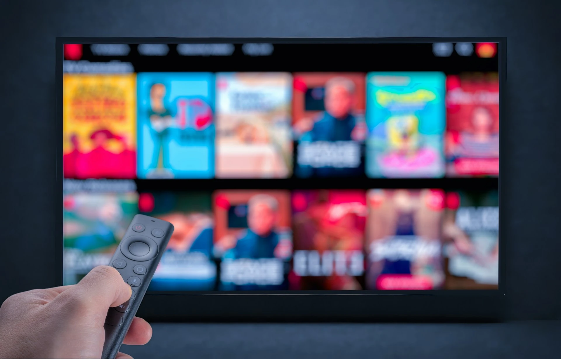 A hand holds a remote control, pointing it at a TV screen showing a streaming service.