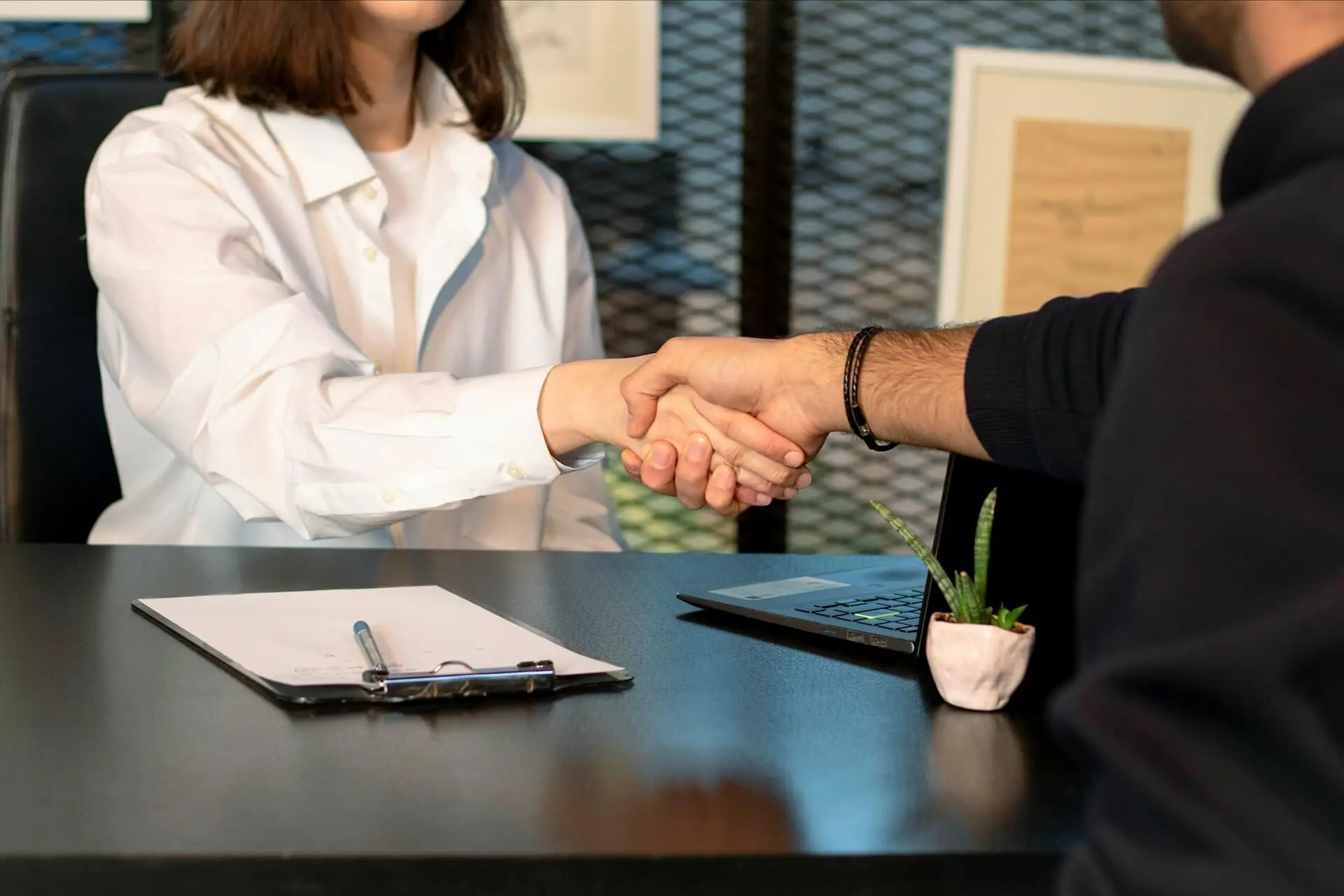 Close-up of a man and woman shaking hands over a dark office desk.