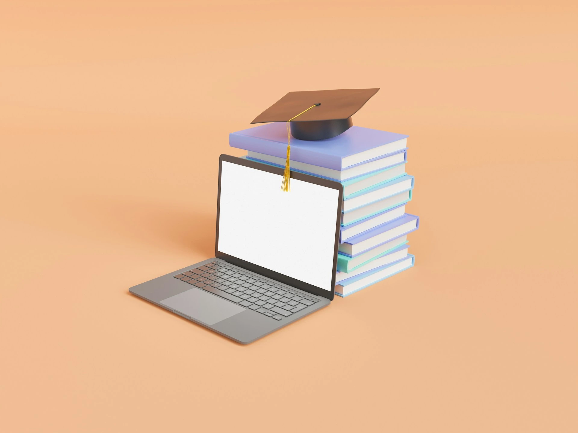 A laptop next to a stack of books topped with a graduation cap.