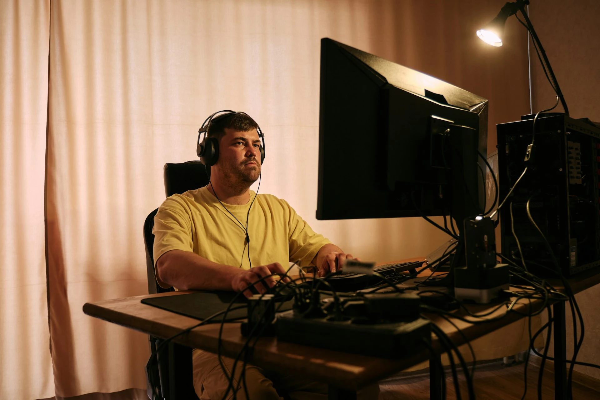 A man wearing over-ear headphones working at a computer desk.