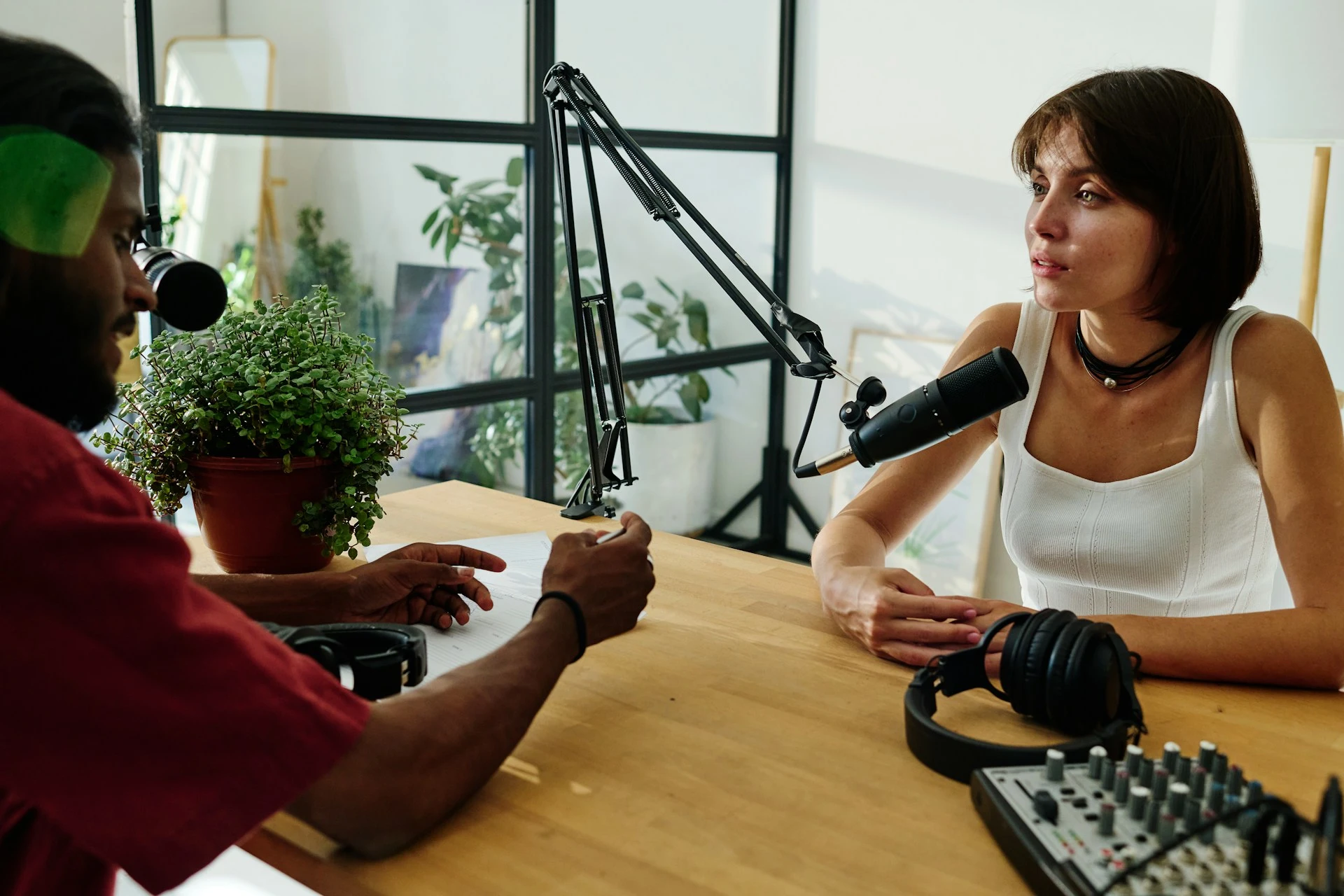 A man and woman recording a podcast interview at a desk with microphones.