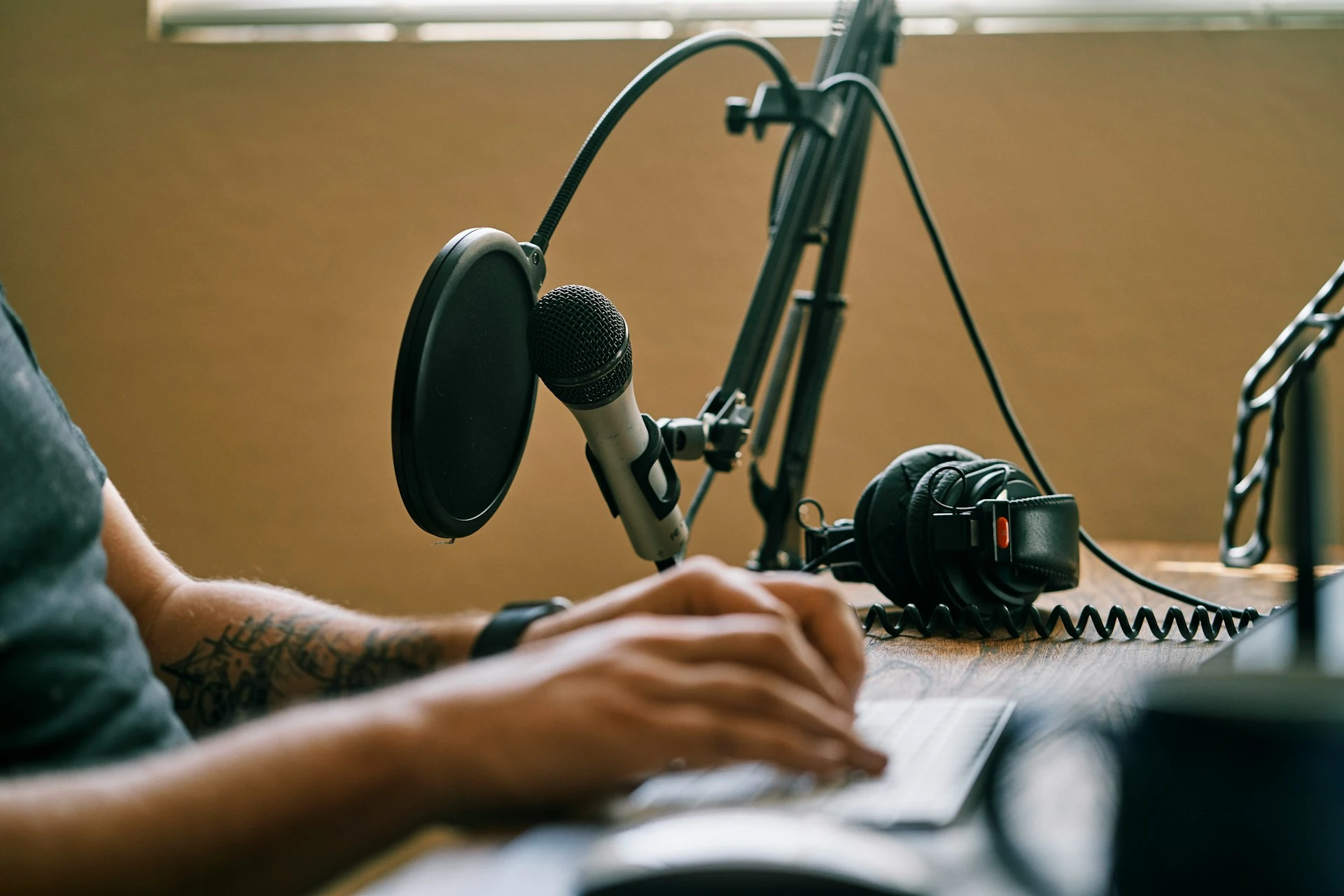A person typing on a keyboard at a desk with professional podcast equipment.