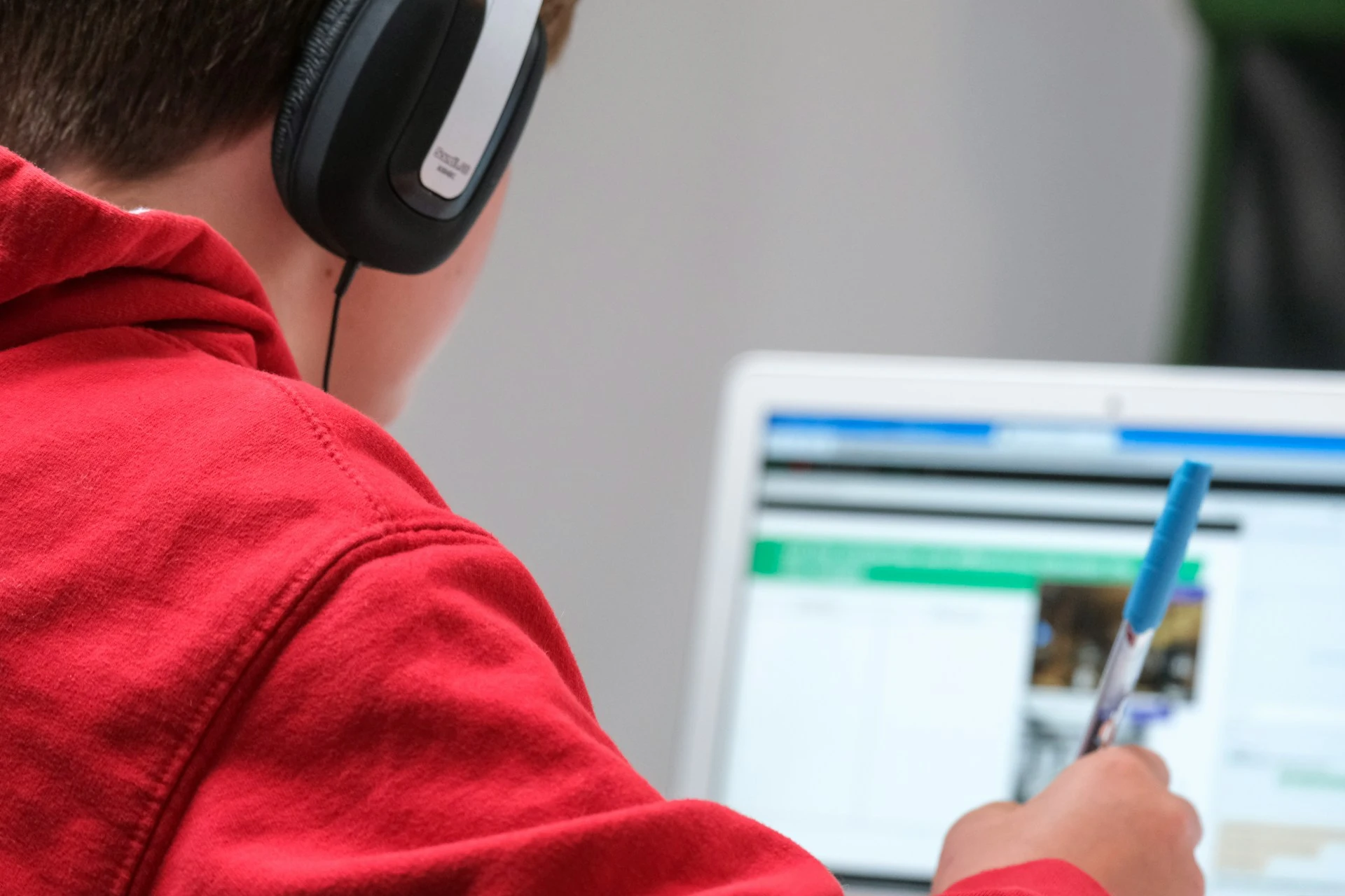  A student wears headphones and uses a pen to follow along with a laptop screen.
