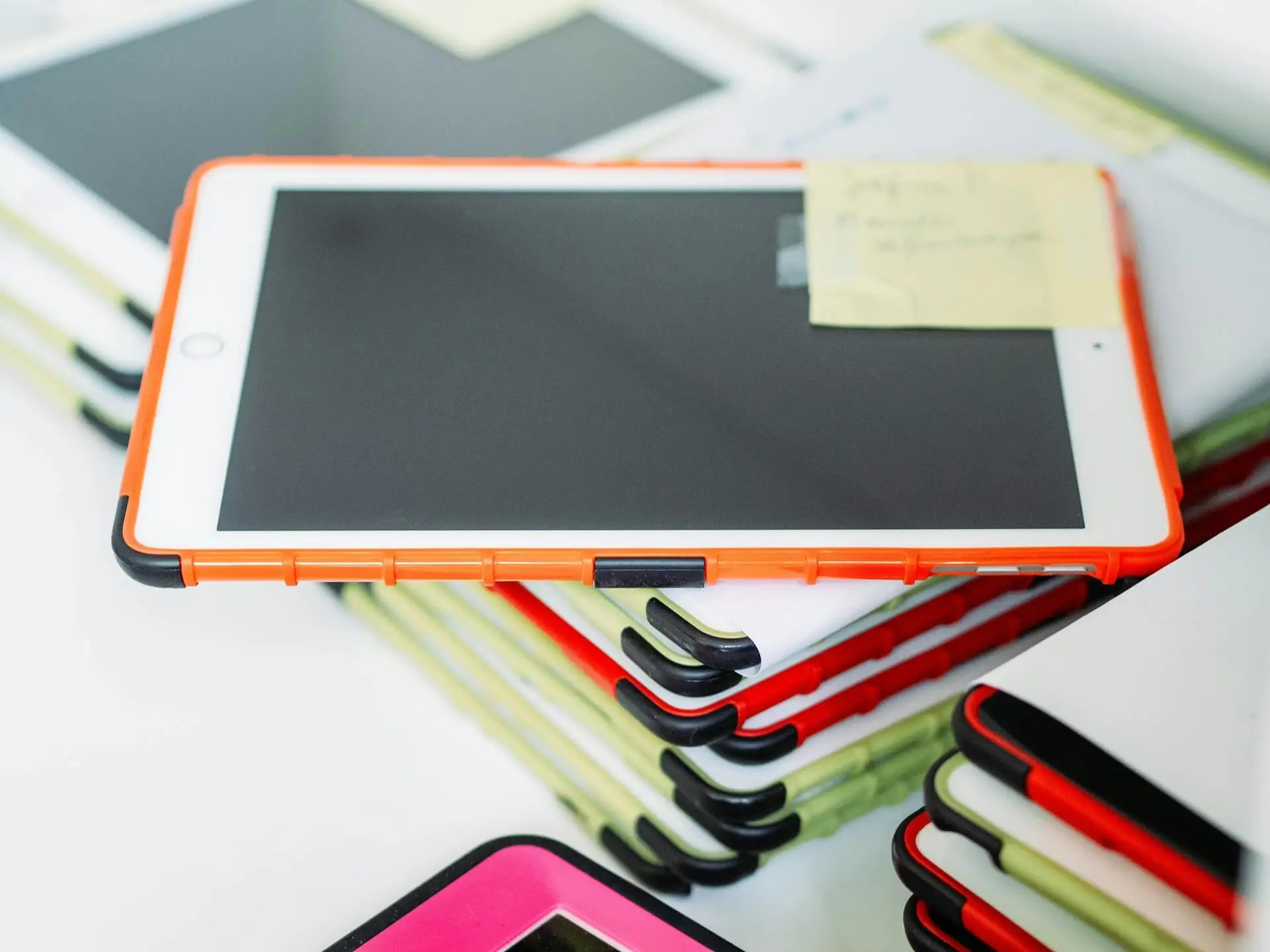 A stack of classroom tablets in protective orange and green cases.