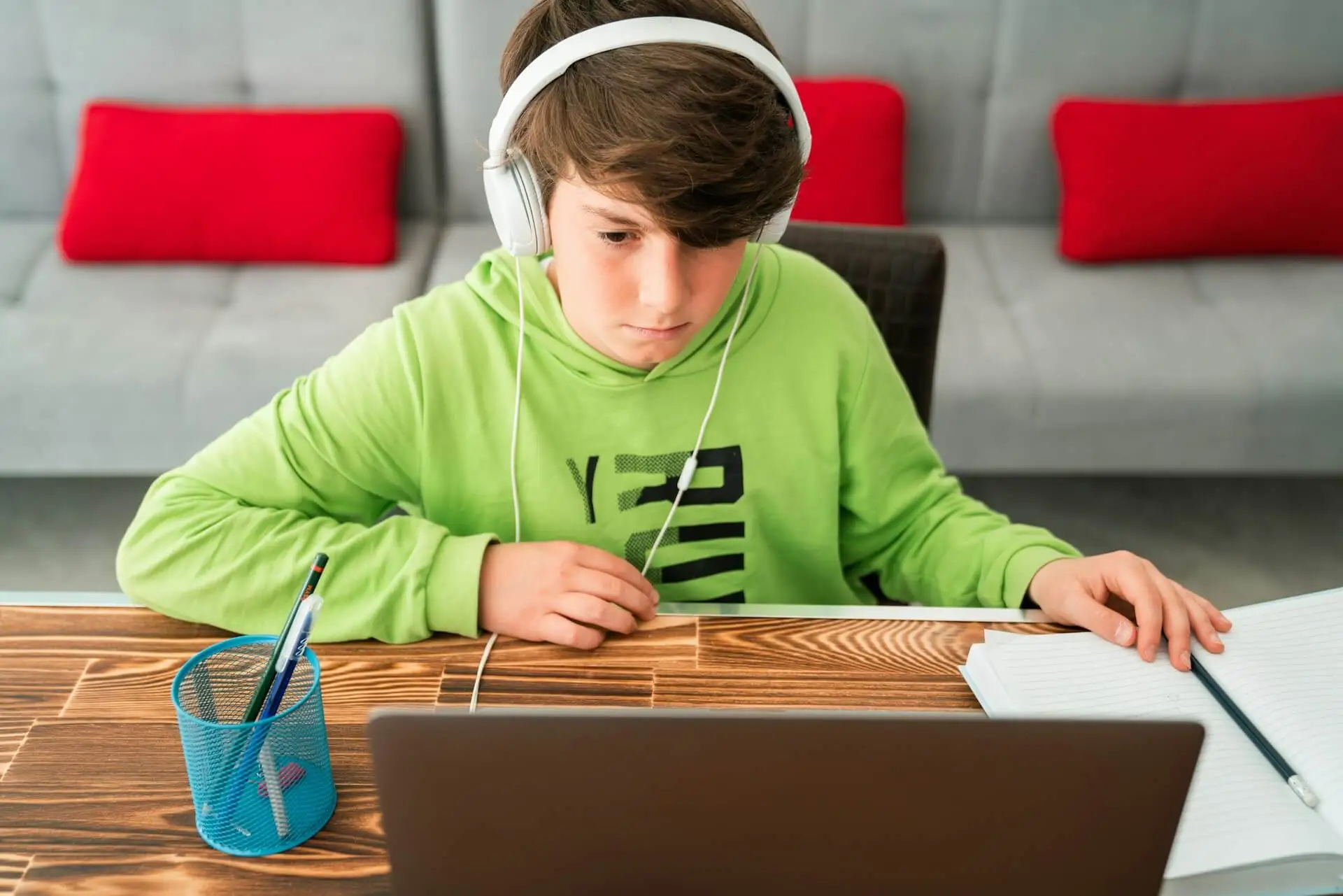 A student wearing headphones focuses on a laptop with an open notebook nearby.