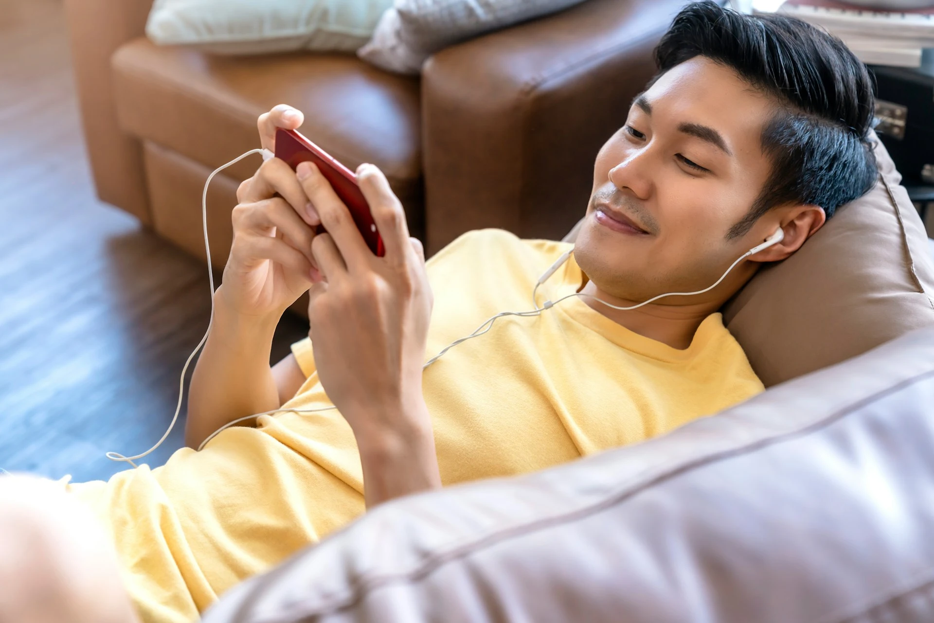 A smiling person is lying on a couch and holding a phone while watching a video.