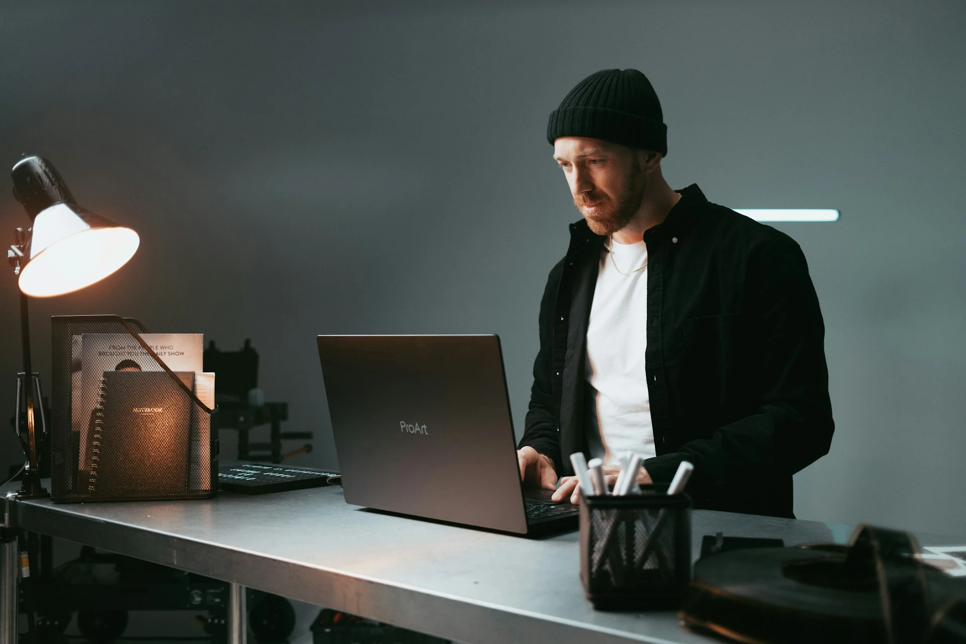 A man working on a laptop at a desk in a dimly lit studio setting.