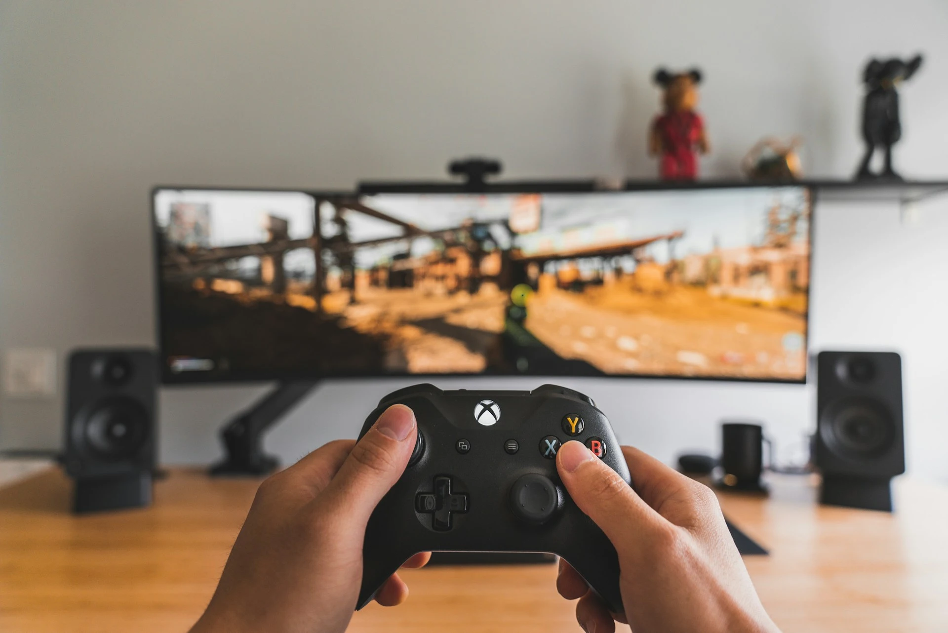 Person holding a black Xbox controller while playing a video game on a wide curved monitor.
