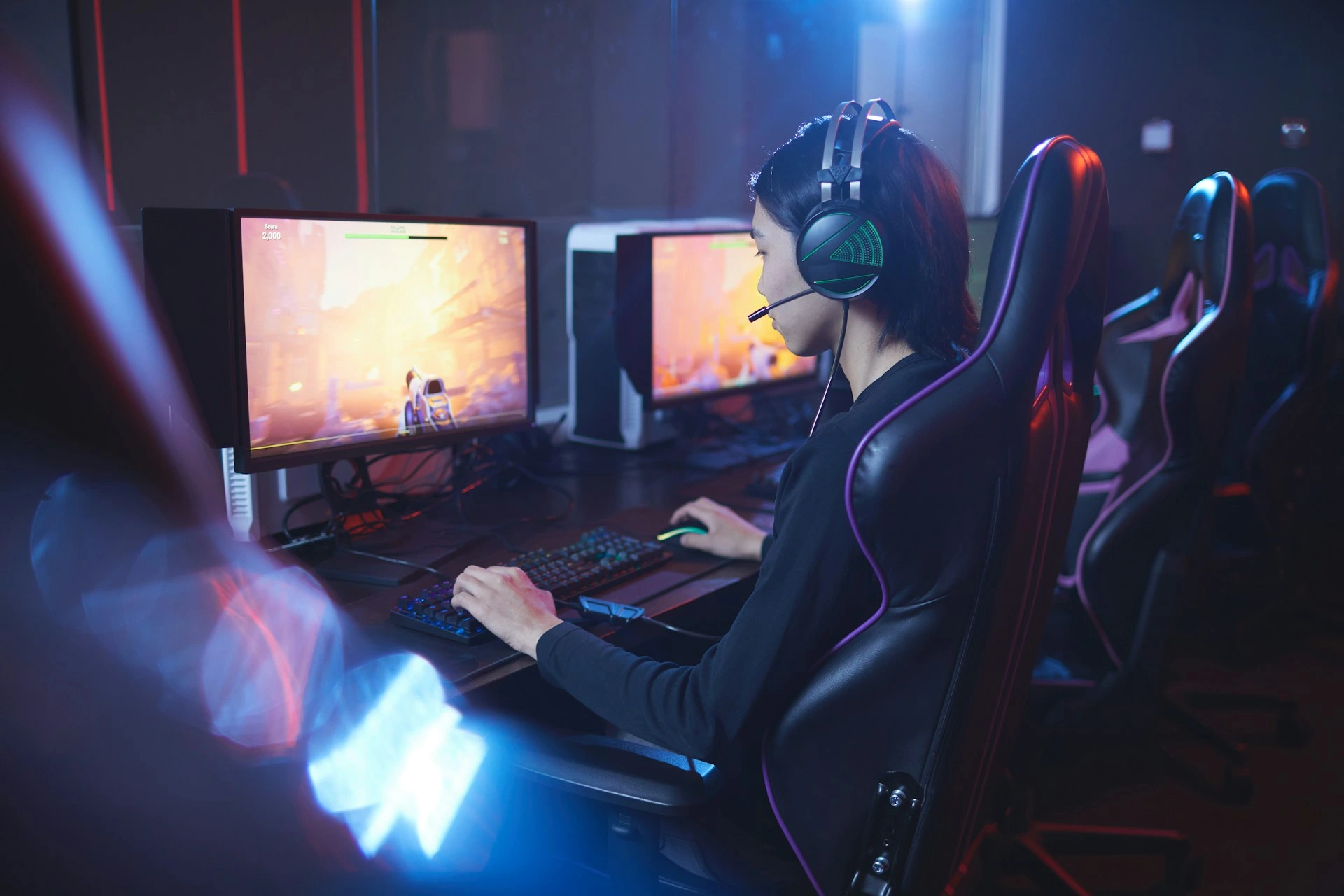 Person wearing a headset playing a computer game on a desktop setup in a gaming room.