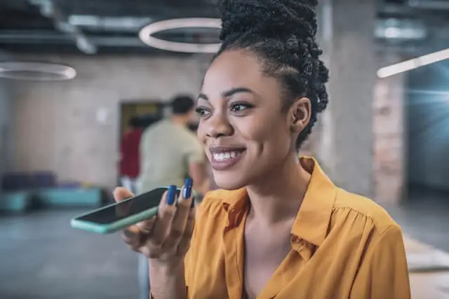  A woman smiles while holding a phone up to her mouth, speaking into it.