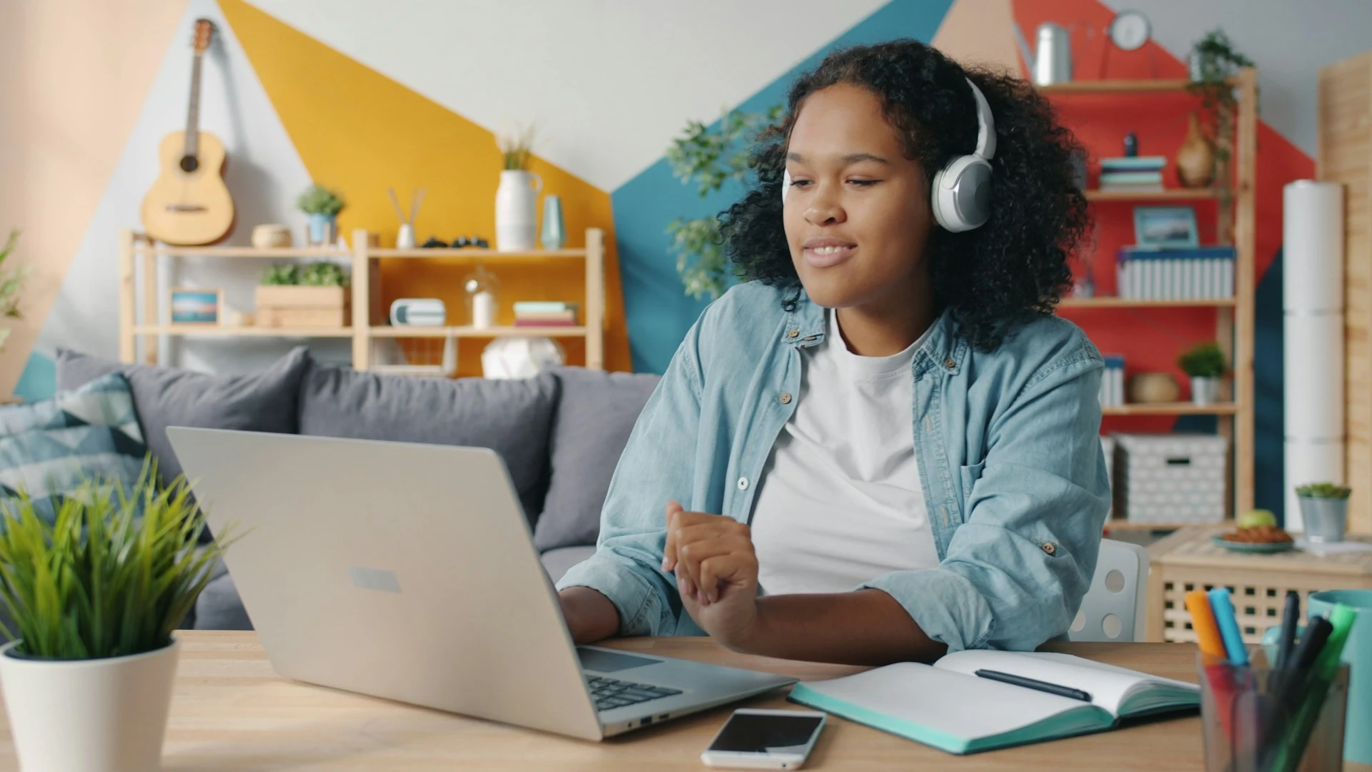  A student wearing headphones smiles while looking at a laptop screen.