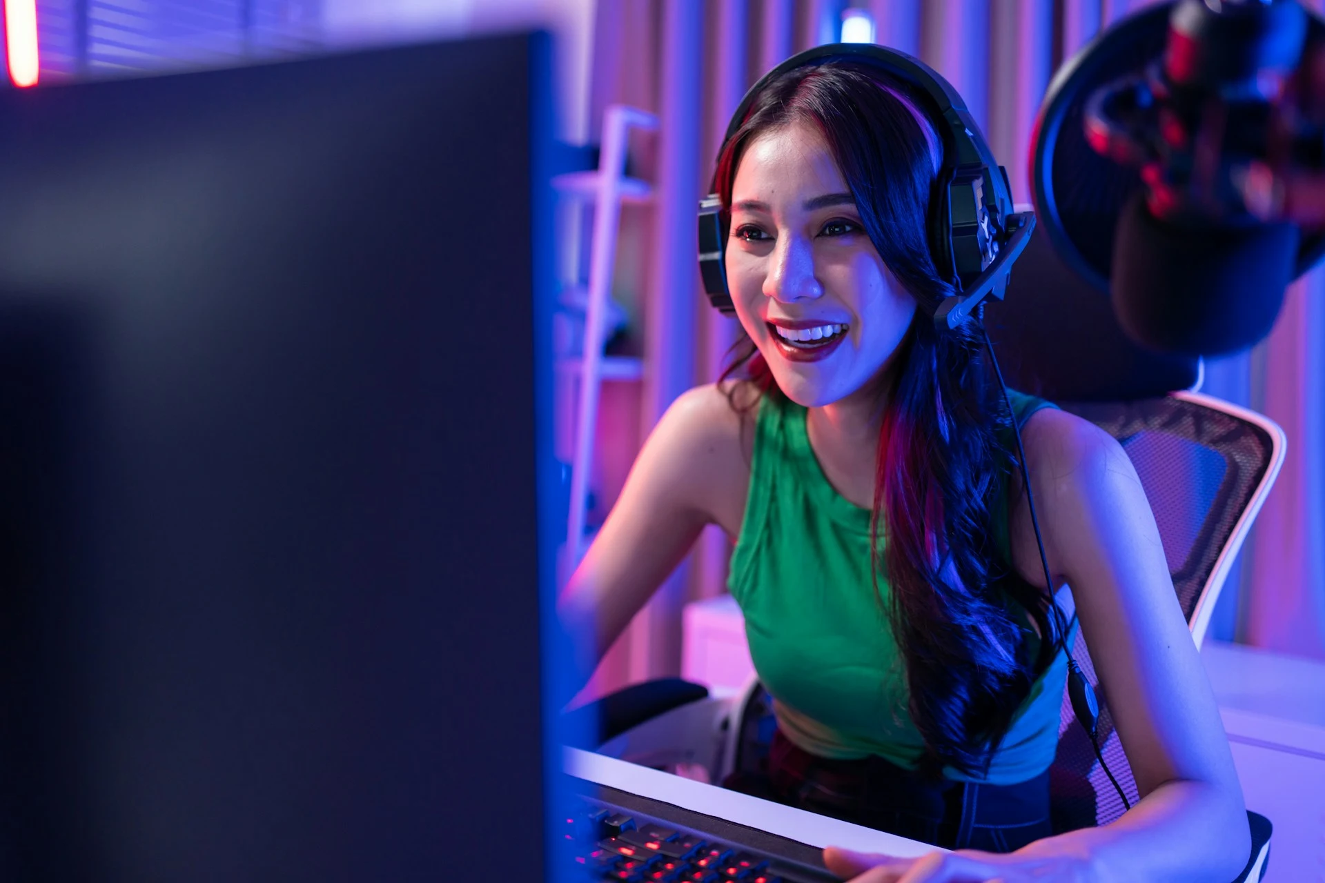 A woman wears a gaming headset and smiles while looking at a computer screen.
