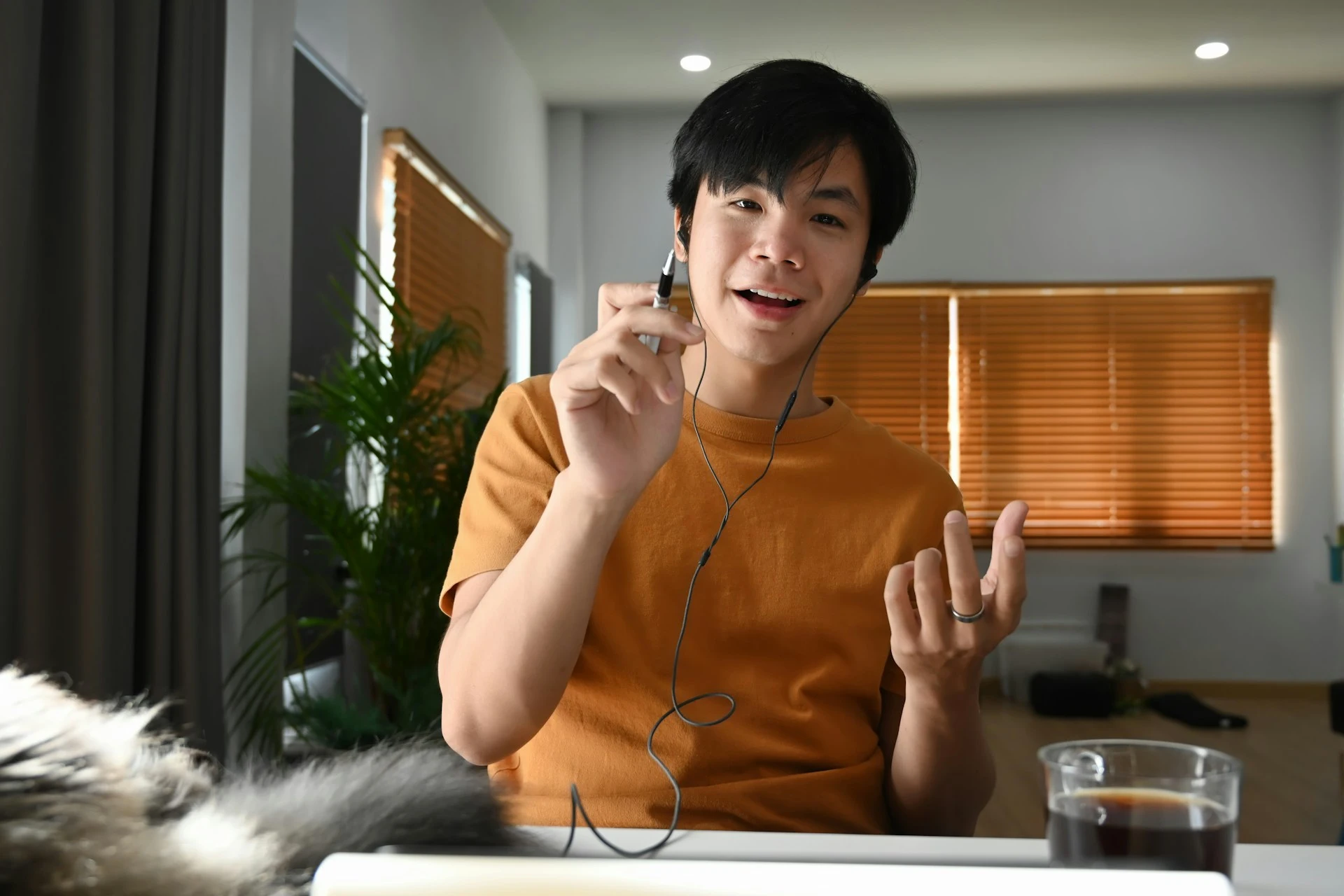 A man wearing wired earphones speaks directly to the camera while gesturing with his hands.