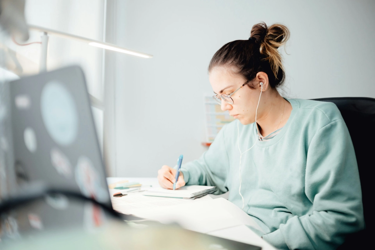 A student taking notes while listening to a lecture on their laptop