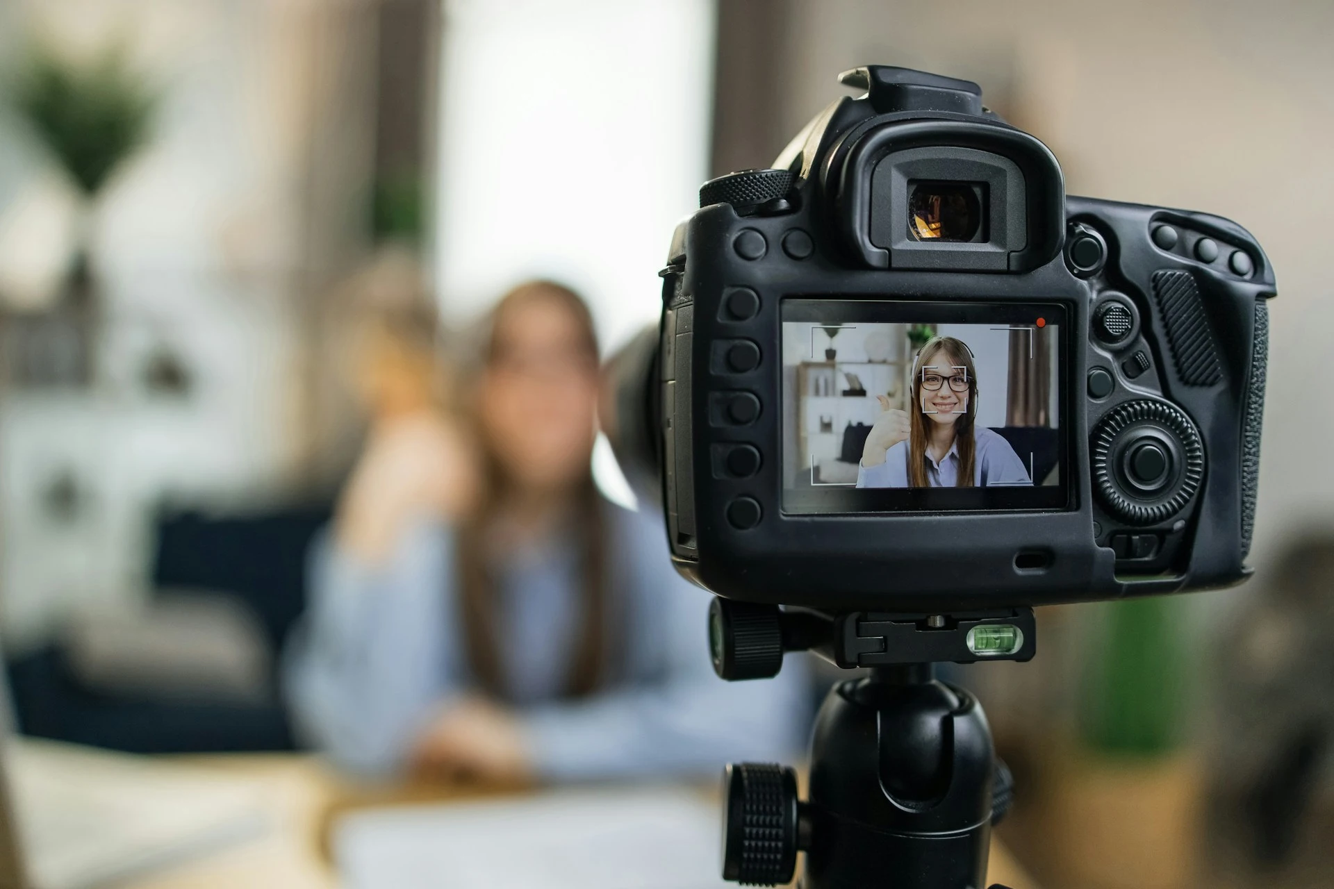 Camera on a tripod recording a woman giving a thumbs-up.