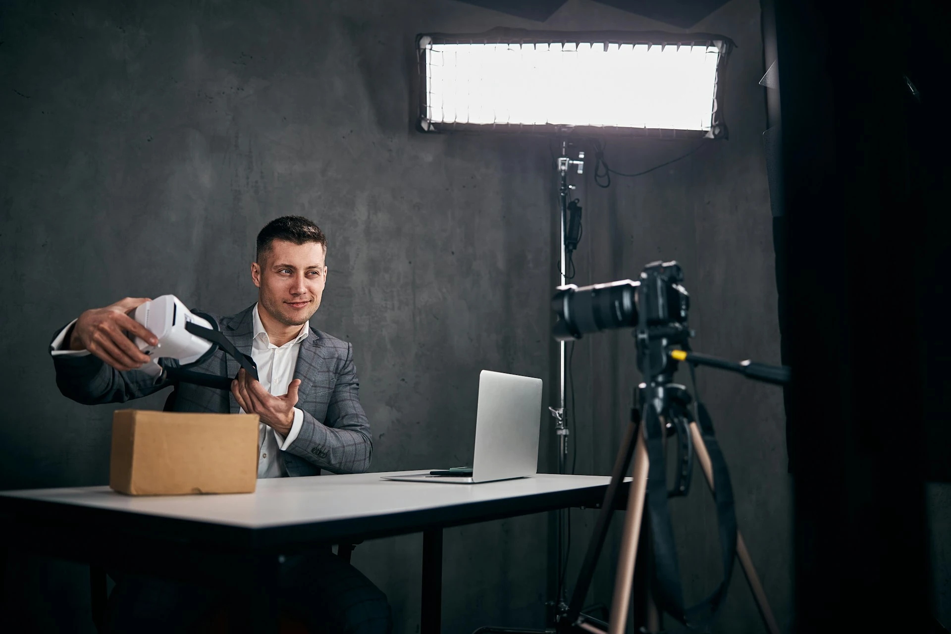 Man presenting a VR headset to a camera on a tripod during a video shoot.