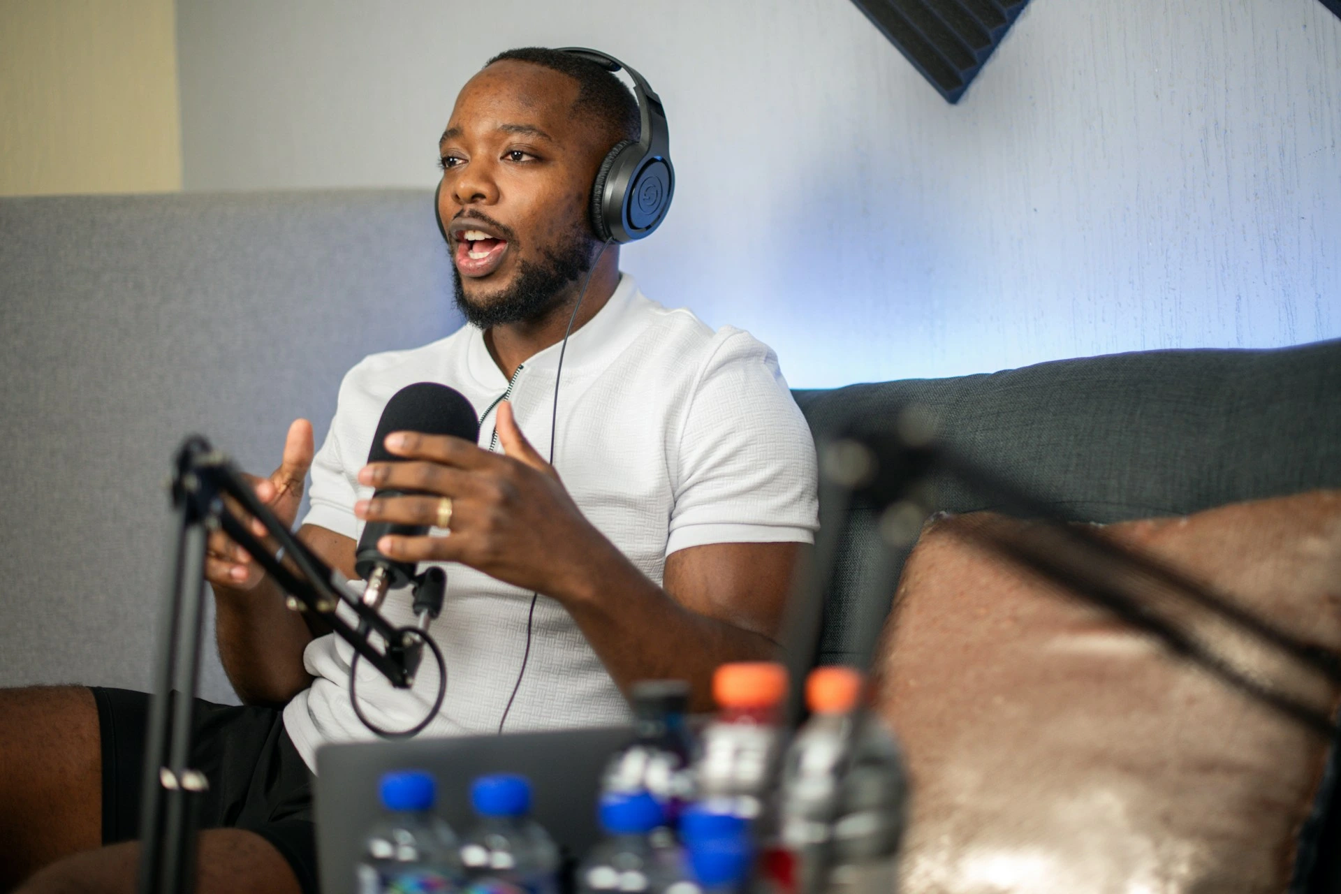 Man wearing headphones speaking into a microphone while sitting on a couch.