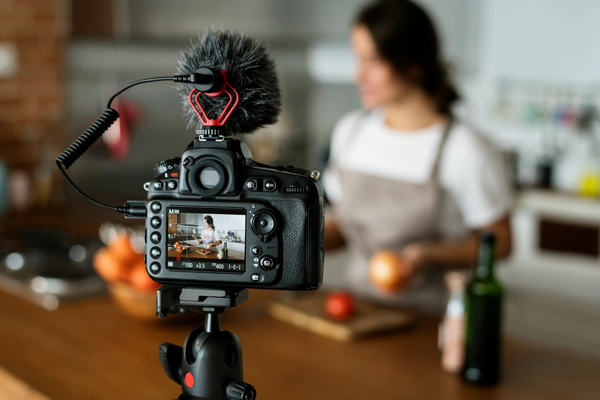 Camera on a tripod filming a woman preparing food in a kitchen.