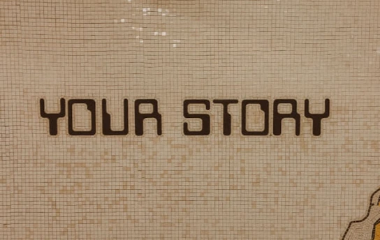 A wall made of tiles having the words your story on it.