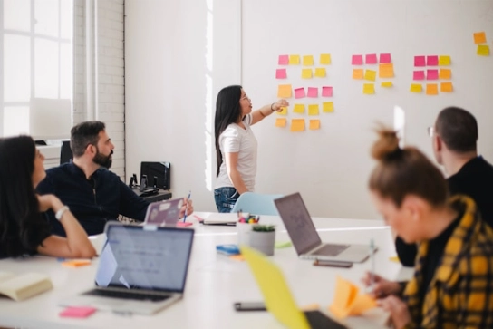 A woman speaking in front of a wall with sticky notes during a business meeting.