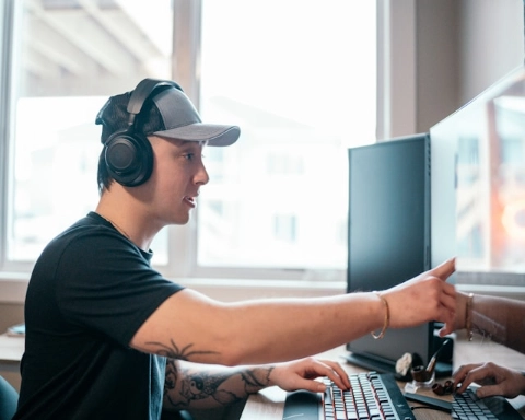 A person wearing headphones and pointing at a computer screen.