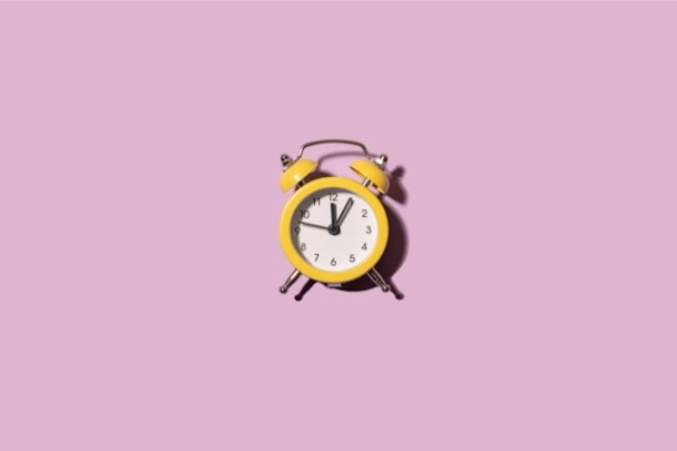 A yellow alarm clock on purple backgound.