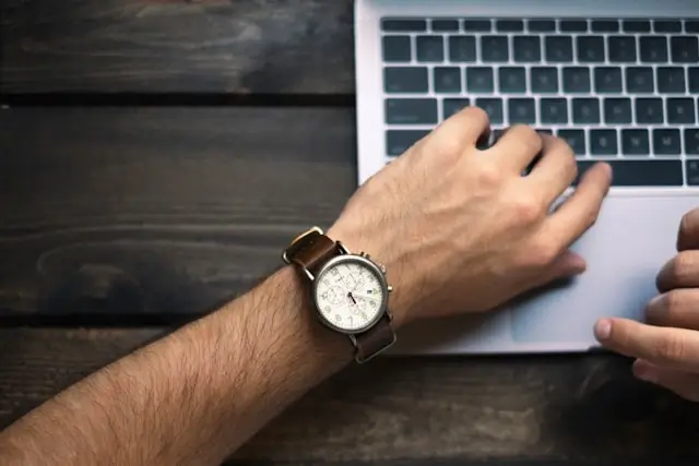 Close-up of a person’s wrist with a watch while using a laptop, signifying the time-consuming aspect of human transcriptions.