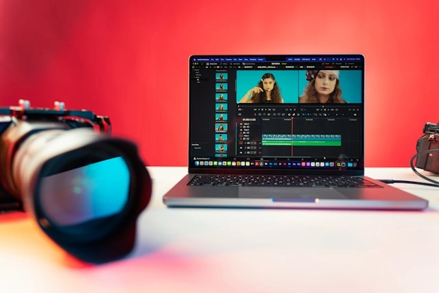 A camera lens and a laptop displaying video editing software on a table.