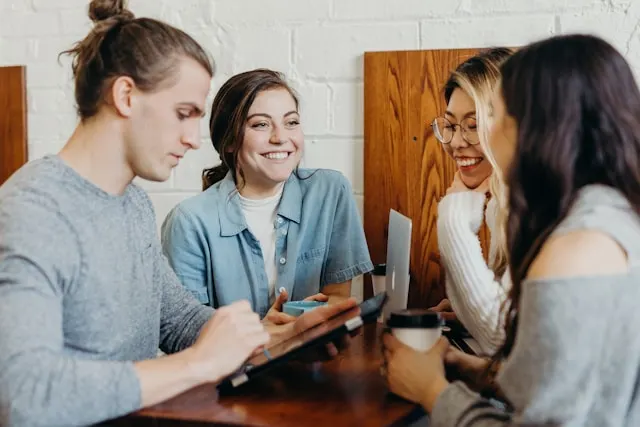 A group of friends chatting while drinking coffee and looking at a tablet.