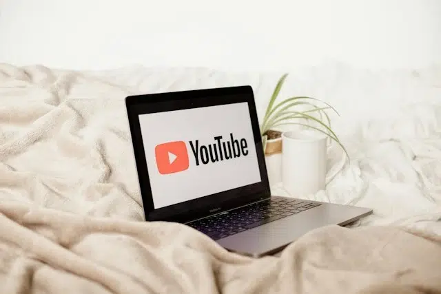 A laptop on a bed displaying the YouTube logo.