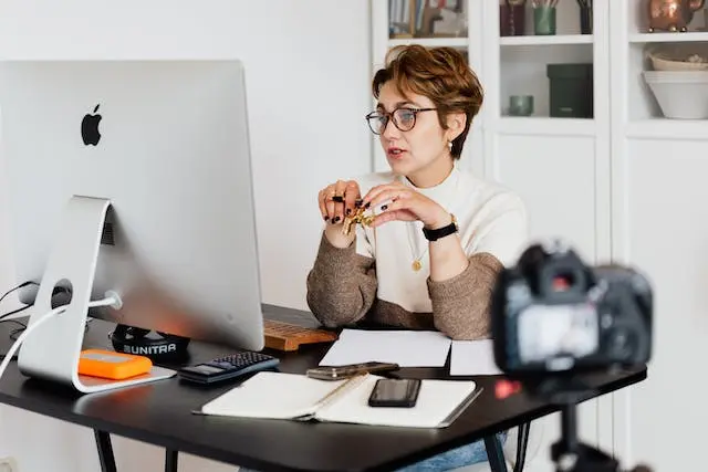 A woman looking at the desktop screen and addressing the camera.