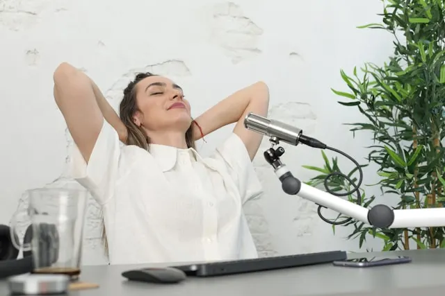 A woman in a white shirt sitting in front of a desk with a microphone.