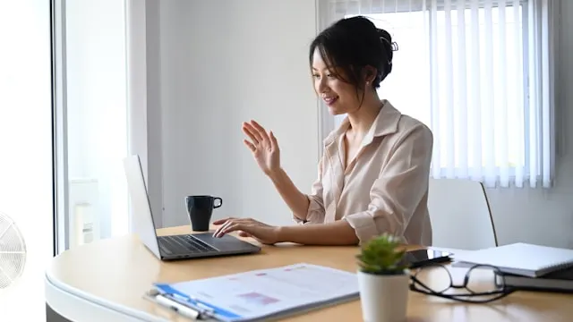 Smiling women in pink shirt waiving at her laptop screen.