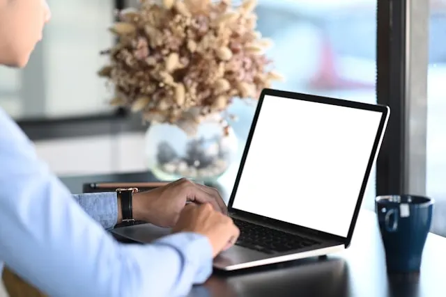 Cropped shot of a young man in blue shirt typing on his laptop.