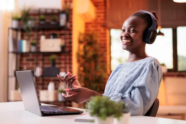 A woman with headphones laughing during a video call.