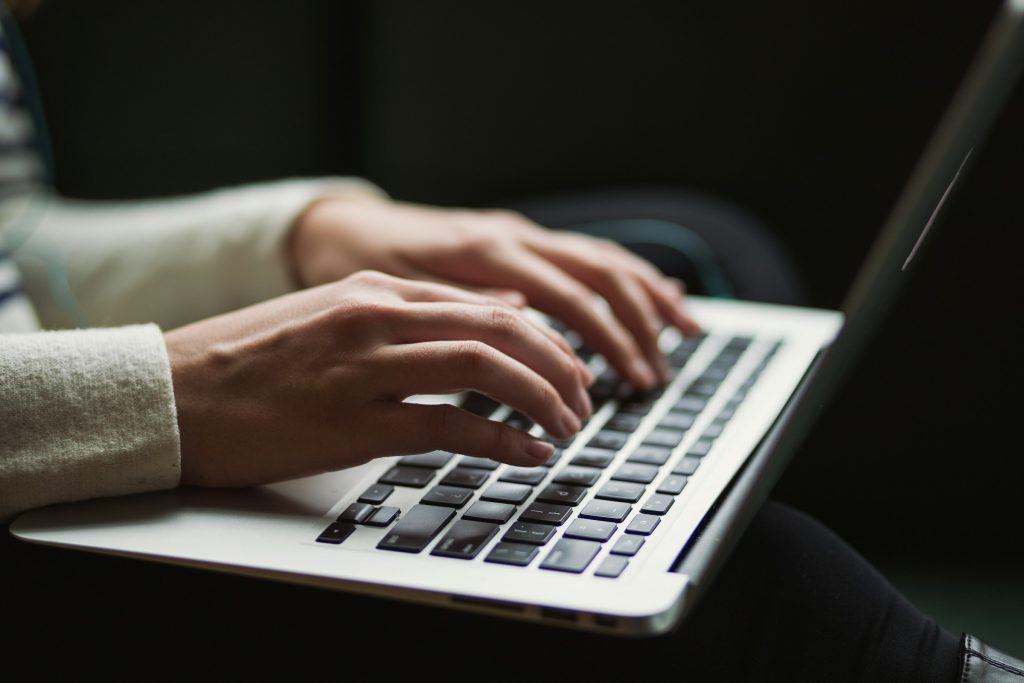 Close-up of a woman's hands typing on a laptop keyboard.