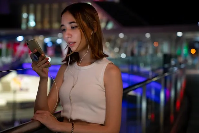 A young woman looking at her phone screen with headphones on.