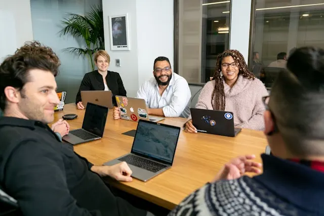 6 people around a table chatting and laughing during a meeting.