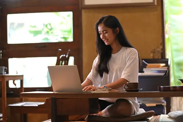 A woman typing on her laptop while sitting at a wooden desk.