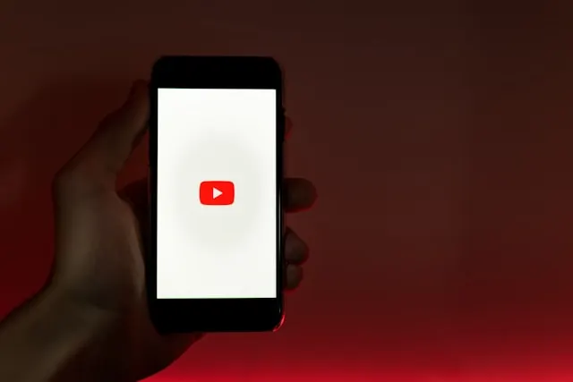 A hand holding a smartphone displaying the YouTube logo.