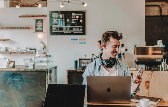 A man at a cafe working on his laptop and using his smartphone.