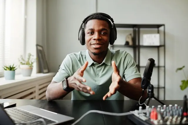 A man with headphones on speaking next to a microphone.