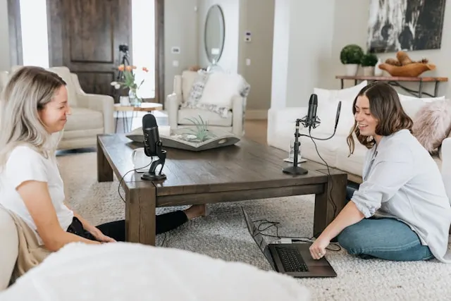 Two women making a podcast together with microphones and a laptop.