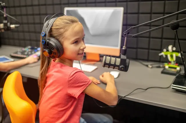 A kid wearing headphones and speaking to a microphone.